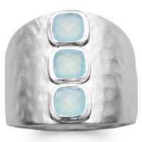 Bague large martelée en argent 925/000 rhodié surmontée de trois véritables pierres d'agate bleue serties clos. L'agate représente l'équilibre et l'harmonie. Elle est symbole de force et de soutien dans les moments difficiles en recentrant les énergies. Pierre d'ancrage à la terre, elle aide à disperser les énergies négatives et confère stabilité et confiance de soi.