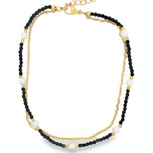 Cette magnifique chaîne de cheville double rang apporte une touche de fraîcheur et d'élégance estivale à votre style. Conçue pour épouser délicatement la cheville, elle combine la durabilité de l'acier et le charme intemporel des perles pour un look à la fois bohème et raffiné. Le bijou se compose de deux chaînes superposées qui créent un effet de superposition parfait. Une fine chaîne en maille forçat dorée, épurée et lumineuse. Un enchaînement de petites perles facettées noires, intercalées de perles blanches plus imposantes à l'aspect marbré ou nacré, encadrées par de petites billes dorées. Dotée d'un fermoir mousqueton sécurisé et d'une chaînette d'extension, elle s'adapte idéalement à toutes les morphologies de chevilles.