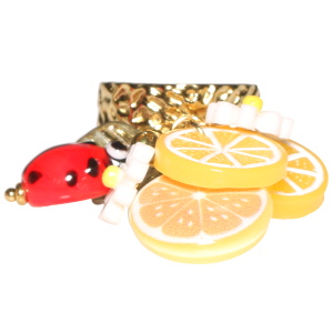 Bague martelée en acier doré avec des tranches d'oranges, une coccinelle et des fleurs de couleur. Taille ajustable.