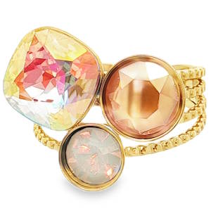 Cette bague est une pièce affirmée qui mise sur le volume et un jeu de lumière chaleureux. Elle allie la robustesse de l'acier doré à l’éclat de cristaux multicolores pour un rendu à la fois bohème et sophistiqué. Le plateau est orné d'une grappe asymétrique de trois pierres, créant un design dynamique qui habille largement le doigt. Une grande pierre de forme carrée aux coins arrondis (coussin). Elle présente un effet aurore boréale avec des reflets changeants allant du jaune pâle au rose fuchsia. Un cristal rond de couleur champagne rose avec une taille facettée nette qui capte la lumière en profondeur. Un cabochon rond plus discret aux reflets opalins et pailletés, apportant une touche de douceur à l'ensemble. Anneau ajustable (ouvert à l'arrière) pour s'adapter parfaitement à toutes les morphologies de doigts.